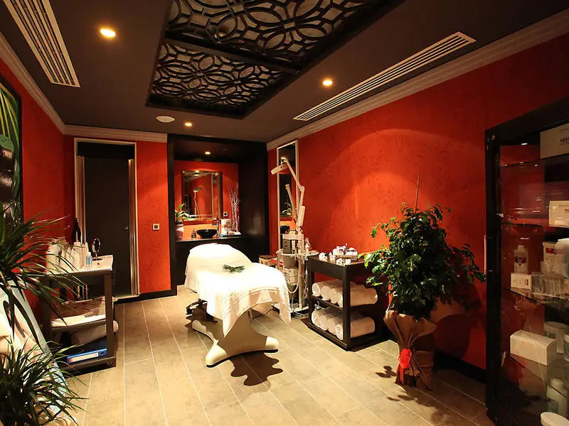 Spa-Behandlungsraum im Rixos Downtown Antalya mit Behandlungsliege, roten Wänden und Pflegeprodukten